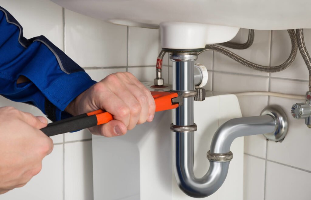 Plumber tightening pipe under bathroom sink with wrench